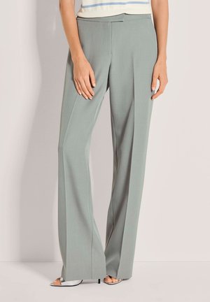 Hellgrüne, weit geschnittene Hose aus glattem Stoff, mit flacher Vorderseite und feiner Bügelfalte. Kombiniert mit einem gestreiften Oberteil und Sandalen.