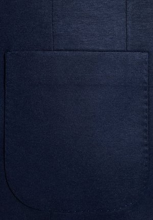 Granatowy materiał z dużą kieszenią naszywaną, gładką teksturą oraz widocznymi szwami i detalami. 