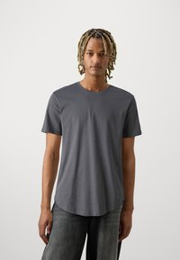 Grijze korte mouw t-shirt van zacht katoen, met een ronde halslijn en een iets verhoogde zoom, gedragen met losse jeans.