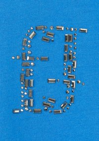 Blauer Stoff mit einem strukturierten Design, auf dem metallische Nieten einen Buchstaben "E" bilden. Die Nieten variieren in Form und Größe und erzeugen einen optisch auffälligen Effekt.