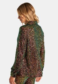 Top de lentejuelas con un cuello tipo camisa. Presenta lentejuelas multicolores en verde, dorado y rojo, mangas largas y un diseño de corte relajado.
