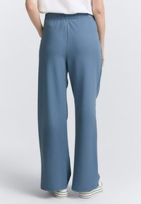 Lichtblauwe wijde broek met een elastische tailleband en een gladde textuur. Heeft een relaxte pasvorm en valt net boven de schoenen.