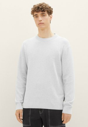 Helles graues Strickpullover mit gerippter Textur, Rundhalsausschnitt und langen Ärmeln, mit geradem Saum und dezentem Branding an der Seite.