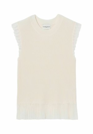 Donna con capelli lunghi e scuri che indossa un top bianco senza maniche con bordi arricciati, gonna nera plissettata, scarpe marroni e tiene una borsa a tracolla bianca.