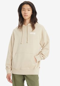 Sudadera beige con un bolsillo frontal, capucha con cordón y logo blanco de "LEVI'S". Fabricada en un tejido suave con un corte holgado y puños acanalados.