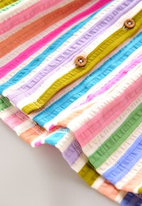 Gros plan sur un tissu côtelé multicolore avec des rayures verticales et des boutons en bois sur le bord d'un vêtement.