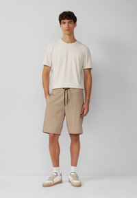 Helles beige Kurzarm-T-Shirt kombiniert mit sandfarbenen Shorts mit elastischem Bund und Kordelzug. Weiße Sneaker mit beigen Akzenten.