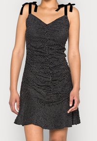 Schwarzes Kleid mit Polka-Dots, tailliertem Oberteil, gerafftem Design und ausgestelltem Saum. Verfügt über Samtschlaufen und einen V-Ausschnitt.