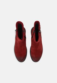 Botines de ante rojo con una textura suave, que presentan detalles de cremallera a ambos lados y puntera redonda. Las suelas de goma negra completan el diseño.