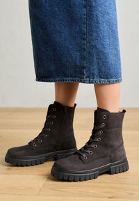 Stivaletti alla caviglia in camoscio marrone scuro con finitura texturizzata, design con lacci e suola in gomma nera a contrasto con un motivo a battistrada spesso.