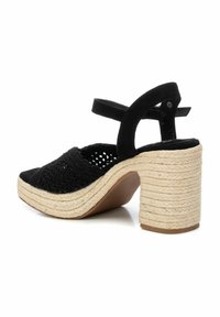 Sándala de tacón de tela negra trenzada con punta abierta, que presenta un talón de cuerda trenzada en color crema y una correa en el tobillo para un ajuste seguro.