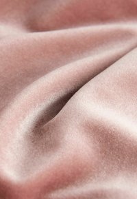 Jemně růžový sametový materiál s mírnými záhyby a hladkou, nadýchanou texturou, která odráží světlo.