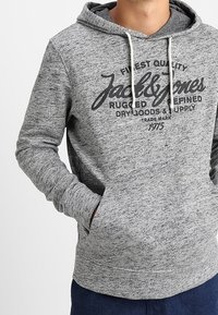 Sudadera gris melange con bolsillo tipo canguro, capucha con cordón y logo impreso. Presenta puños y dobladillo acanalados para un ajuste y comodidad óptimos.