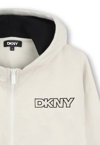 Sweatshirt à capuche zippé crème avec doublure intérieure noire et logo DKNY brodé, comprenant un col côtelé et une texture lisse.