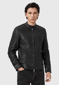 Zwarte leren motorjack met een hoge kraag, ritssluiting aan de voorkant en zijzakken. Glad textuur en een aangesloten ontwerp.