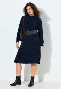 Donkerblauwe gebreide jurk met lange mouwen, zijsplits, een geribbelde halslijn en een brede zwarte riem. Gepaard met zwarte enkellaarsjes.