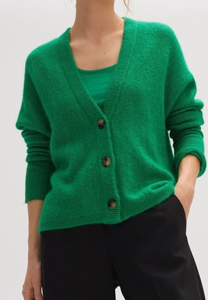 Cardigan oversize vert en tissu doux, avec un col en V, des poignets côtelés et trois grands boutons marron sur le devant.