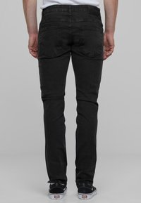 Crne trake slim-fit traperice s glatkom teksturom, sadr�že dva stražnja džepa i oznaku na pojasu. Uparene s crno-bijelim tenisicama.