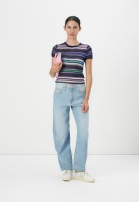 Gestreiftes, kurzärmliges Oberteil in Marineblau mit lila, grünen und weißen Streifen; hellblaue, locker sitzende Jeans; rosa Clutch; weiße Sneakers.