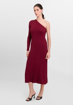 Bordeaux ribbet strikkjole med asymmetrisk design, der har en langærmet og en midtlang nederdel. Glat tekstur, minimalistisk stil.