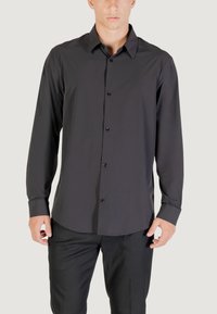 Camicia nera a maniche lunghe con bottoni realizzata in tessuto liscio. Caratterizzata da un colletto classico, bottoni frontali e una vestibilità su misura. I pantaloni non sono visibili.