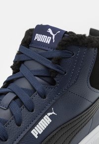 Tumes nahkhi kõrge Greenville tennis, millel on mustad aktsendid, tekstureeritud pind, karvane krae ja valge Puma logo külgedel ja keelel.