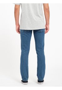 Vaqueros de mezclilla azul con un corte ajustado, que presentan un diseño clásico de cinco bolsillos y detalles de costura sutiles, combinados con una camiseta gris.