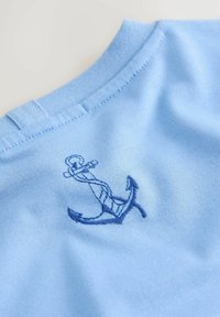 Svetlo modra bombažna tkanina ima na prsih modro vezen sidro, z gladko teksturo in klasičnim okroglim izrezom.