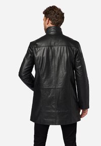 Black leather coat with a high collar, characterized by a smooth texture and stitched panel details on the back and sleeves.