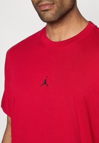 Κόκκινο βαμβακερό T-shirt με στρογγυλή λαιμόκοψη και κοντά μανίκια, με μαύρο λογότυπο Jumpman στο στήθος. Λείος υφασμάτινος ιστός.
