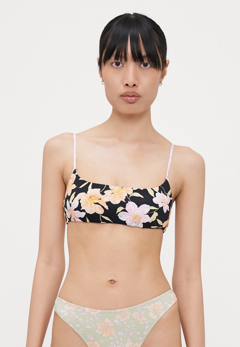 Mønstret bikini topp med blomsterdesign på svart bakgrunn, tynne stropper, og matchende blomstermønstret bunn i lysegrønn.
