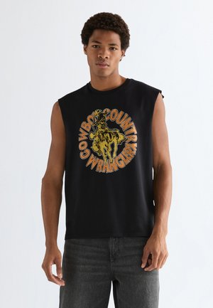Junger Mann trägt ärmelloses schwarzes Shirt mit vintage-stilisiertem Motiv eines Cowboys auf einem Pferd und dem Text "Cowboy Country Wrangler".