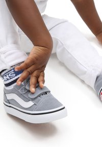 Grå mockasinsneaker med vita detaljer, svart sula och kardborreband. Bärs med marinblå och vita randiga strumpor och vita jeans.