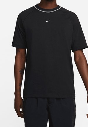 Osoba nosząca czarną koszulkę Nike z krótkim rękawem i małym białym logo Swoosh umieszczonym na środku pod linią dekoltu.