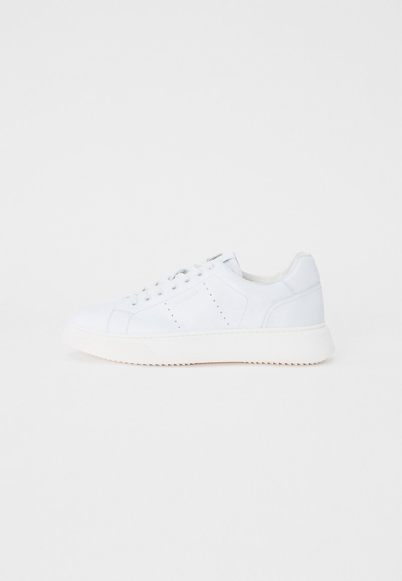 Fehér bőr sportcipő sima textúrával, hat fűzőlyukkal, finom perforációkkal az oldalán és kontrasztos fehér gumitalppal.