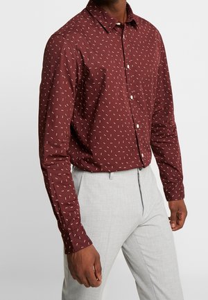 Man wearing a long-sleeve maroon shirt with small white patterns tucked into light gray dress pants.