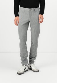 Pantalones de raya diplomática grises con corte ajustado, cierre de botón y bolsillos laterales, combinados con zapatillas blancas con acentos negros.
