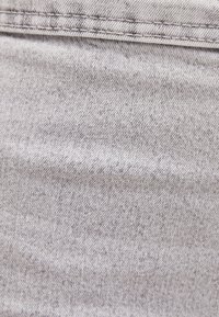 Grått tyg med en subtil diagonal textur och en lätt melerad mönstring. Synlig sömnad längs den övre kanten. Slätt och smidigt material.