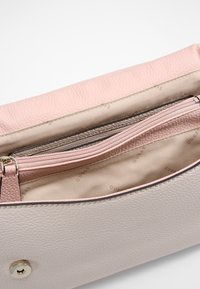 Portefeuille en cuir rose clair et beige avec des compartiments zippés et ouverts, doublure intérieure en tissu beige et fermeture à bouton-pression.