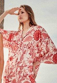 Kimono con estampado floral en tejido suave y ligero. Presenta patrones botánicos rojos sobre un fondo crema. Mangas sueltas y fluidas, y un corte relajado.