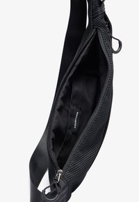 Borsa a tracolla nera con un esterno in rete, chiusura con zip e interno in tessuto liscio. Presenta un'etichetta con la scritta "YOURTURN" all'interno.