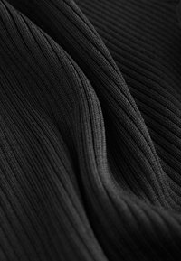 Gros plan d’un tissu côtelé noir avec une texture tricotée verticale et des plis doux créant des lignes courbes et des ombres.