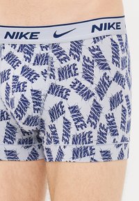 Nike boxer alsónadrág világoskék anyagból, sötétkék absztrakt levélmintával, és passzoló rugalmas derékpánttal, amelyen a márkaneve is szerepel.