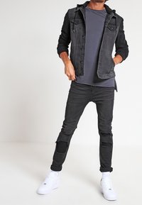 Czarna kurtka dżinsowa z kapturem, w połączeniu z szarą koszulką i podartymi czarnymi dżinsami. Białe trampki dopełniają strój.