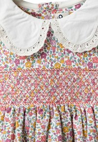 Vestido floral con cuello de encaje blanco, cintura fruncida rosa y falda plisada. Presenta flores multicolores sobre un fondo blanco.