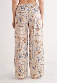 Pantaloni a gamba larga realizzati in tessuto leggero con uno sfondo beige. Presentano motivi floreali e paisley nei colori blu e ruggine. Vita elastica.