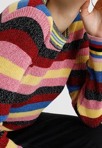 Knitted sweater featuring bold horizontal stripes in pink, red, blue, yellow, and black. Ribbed neckline and cuffs. Soft texture.
