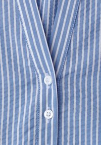 Tissu rayé vertical bleu et blanc avec deux boutons blancs cousus, montrant un gros plan de l'avant d'une chemise boutonnée.