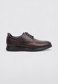 Zapato de cuero marrón con un acabado suave, punta redonda y suela de goma negra. Presenta cierre de cordones y un color interior en contraste.