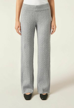 Pantalones de punto acanalado en gris claro de pierna ancha con una superficie texturizada y cintura elástica, combinados con zapatos negros de punta cuadrada.